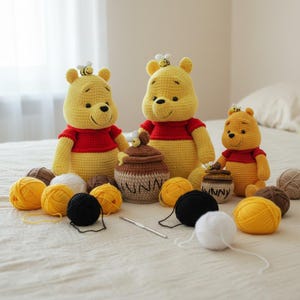May include: Handmade crochet Winnie the Pooh dolls in yellow and red, with a honey pot and yarn balls in yellow, black, white, and brown. A crochet hook is also present. The dolls have a bee on their heads.
