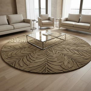 May include: A large, circular, brown rug with a leaf design is the focal point of a living room. A glass-topped coffee table with a silver metal frame sits on the rug. Beige sofas and chairs are arranged around the rug, creating a seating area.