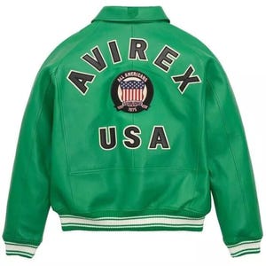 K&ouml;nnte beinhalten: Gr&uuml;ne Lederjacke mit dem Wort "AVIREX" auf dem R&uuml;cken, &uuml;ber einem runden Aufn&auml;her mit der amerikanischen Flagge und den Worten "ALL AMERICANS ESTABLISHED 1975". Das Wort "USA" steht darunter. Die Jacke hat einen wei&szlig;-gr&uuml;nen gestreiften Saum.