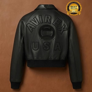 May include: Black leather bomber jacket with the word "AVIREX" and "USA" embossed on the back. The jacket has a ribbed hem and cuffs, a collar, and a "Best Seller" sticker.