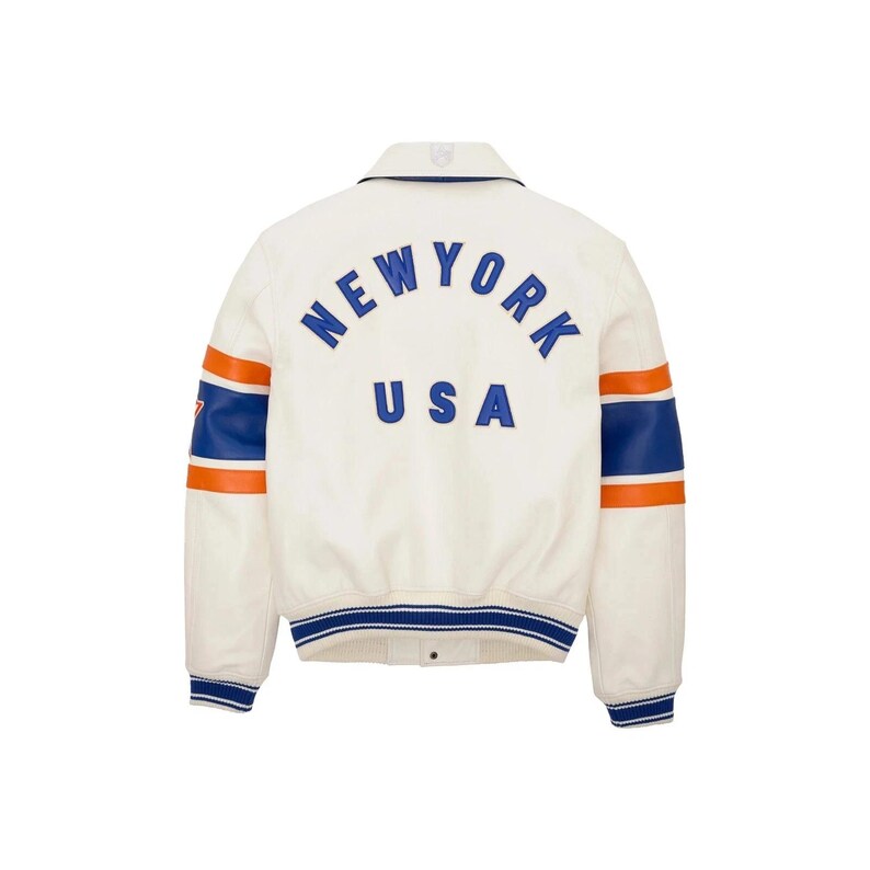 K&ouml;nnte beinhalten: Cremefarbene Collegejacke mit "NEW YORK USA" in blauen Buchstaben auf dem R&uuml;cken. Die &Auml;rmel haben blaue und orangefarbene Streifen. Die Jacke hat einen blau-wei&szlig; gestreiften Kragen und B&uuml;ndchen.