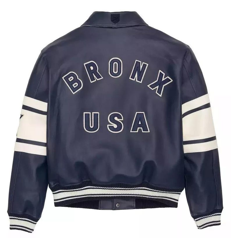 K&ouml;nnte beinhalten: Marineblaue Bomberjacke mit wei&szlig;en Streifen auf den &Auml;rmeln und dem Text "BRONX USA" in wei&szlig;er Schrift auf dem R&uuml;cken. Die Jacke hat einen gerippten Kragen und B&uuml;ndchen.