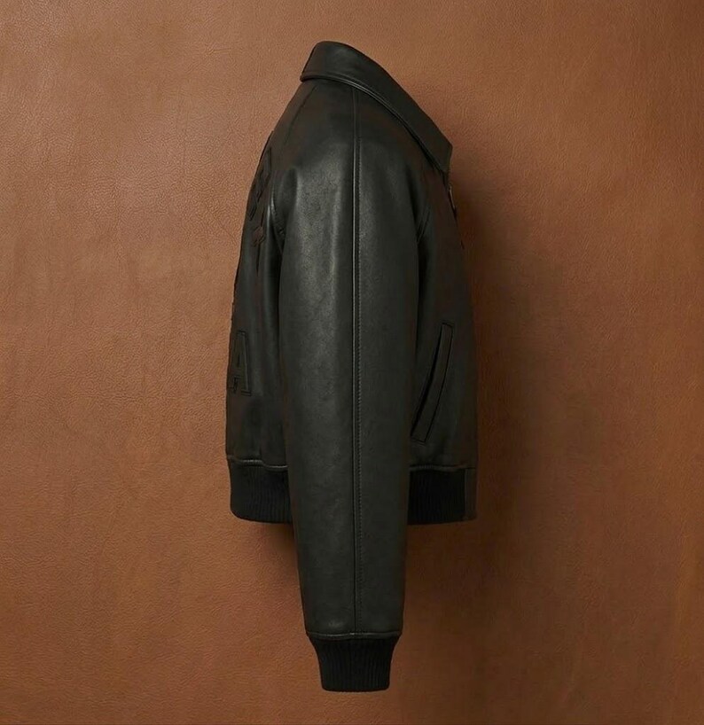 May include: Black leather bomber jacket with a ribbed collar and cuffs. The jacket has a zipper closure and a small pocket on the front. The jacket is a classic style and is suitable for various occasions.