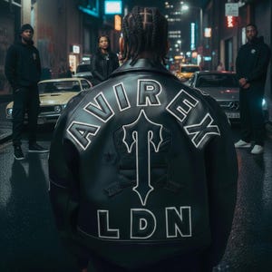 May include: A black leather jacket with white lettering and a logo on the back. The jacket says "AVIREX LDN" in white block letters. The image is taken on a city street at night, with cars and people in the background.