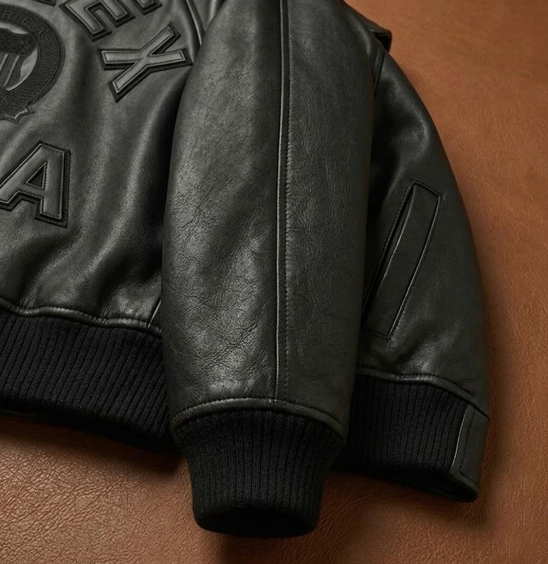 May include: Black leather bomber jacket with a ribbed knit collar and cuffs. The jacket features embroidered lettering on the chest. The sleeves have a classic bomber jacket design with a pocket on the left sleeve.