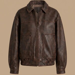 May include: A brown leather jacket with a zip-up front, two front pockets, and a collared neckline. The jacket has a bomber-style design with ribbed cuffs and hem. The leather has a distressed appearance, giving it a vintage look.