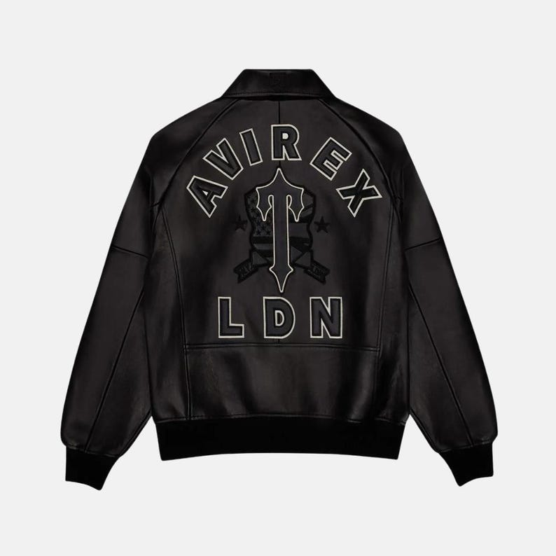 K&ouml;nnte beinhalten: Schwarze Lederjacke mit dem wei&szlig;en Schriftzug "AVIREX LDN" auf dem R&uuml;cken. Die Jacke hat einen klassischen Bomberstil mit geripptem Kragen und B&uuml;ndchen. Das Design beinhaltet ein stilisiertes Emblem.