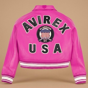 May include: A bright pink leather jacket with the word "AVIREX" across the back in black and white lettering. Below the word "AVIREX" is a circular patch with the words "ALL AMERICANS" and "ESTABLISHED 1975". The word "USA" is below the patch. The jacket has white and pink striped cuffs and hem.