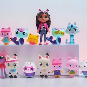 Può includere: Una collezione di statuette di Gabby's Dollhouse, con una bambola centrale con capelli scuri e giacca rosa, circondata da vari personaggi a tema gatto dai colori vivaci. Le statuette sono disposte su una superficie bianca su uno sfondo pastello.