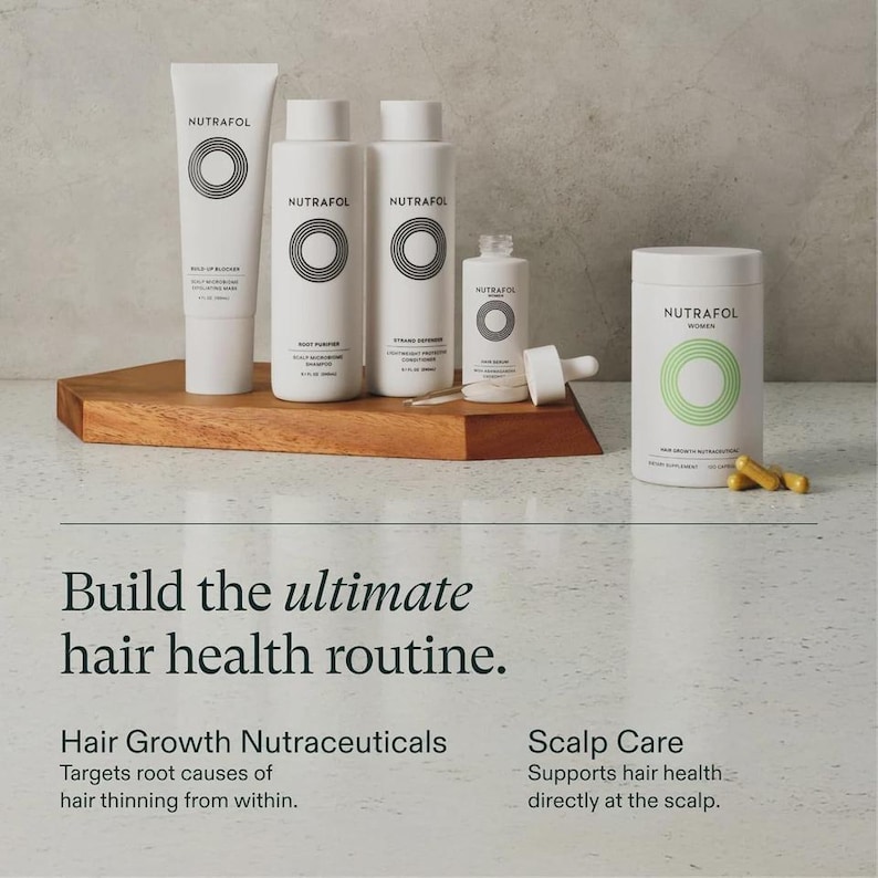 May include: A collection of white NUTRAFOL hair health products, including a tube, bottles, and a jar with capsules, arranged on a wooden surface. The products feature a circular design and the text "NUTRAFOL". The image also includes the text "Build the ultimate hair health routine."