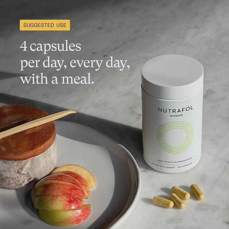 May include: A white cylindrical bottle of Nutrafol Women hair growth nutraceuticals with a light green design. The image also shows four capsules, sliced apples, and text that reads "4 capsules per day, every day, with a meal."