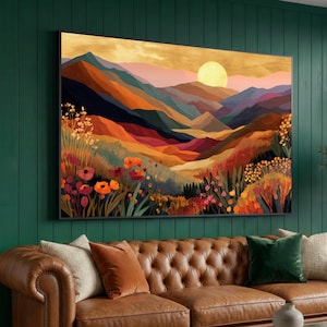 Puede incluir: Una gran pintura de paisaje enmarcada que representa una cordillera bajo una puesta de sol dorada. La obra de arte presenta colores vibrantes, incluyendo naranja, rojo y púrpura, con flores silvestres en primer plano. La pintura cuelga sobre un sofá de cuero marrón.