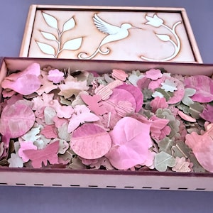 Puede incluir: Una caja de madera con tapa que presenta un colibrí y un diseño floral. La caja está llena de recortes en forma de hojas rosas y verdes. La caja está abierta, revelando el contenido. La tapa está parcialmente abierta.