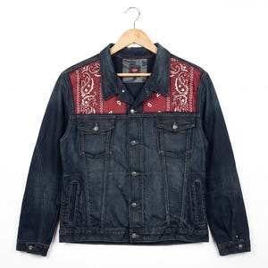 Può includere: Giacca di jeans blu scuro con pannelli sulle spalle con motivo paisley rosso. La giacca ha una chiusura con bottoni, due tasche sul petto e due tasche laterali. La giacca è appesa a una gruccia di legno.