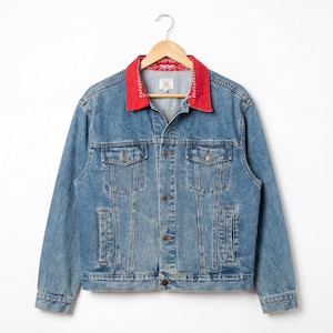 May include: A light blue denim jacket with a red bandana-print collar. The jacket has a classic design with button closures, chest pockets, and side pockets. It hangs on a wooden hanger against a white background.