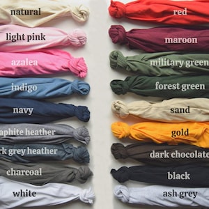 May include: Folded t-shirts in a range of colours, such as natural, light pink, azalea, indigo, navy, graphite heather, dark grey heather, charcoal, white, red, maroon, military green, forest green, sand, gold, dark chocolate, black, and ash grey. Each shirt is labelled.