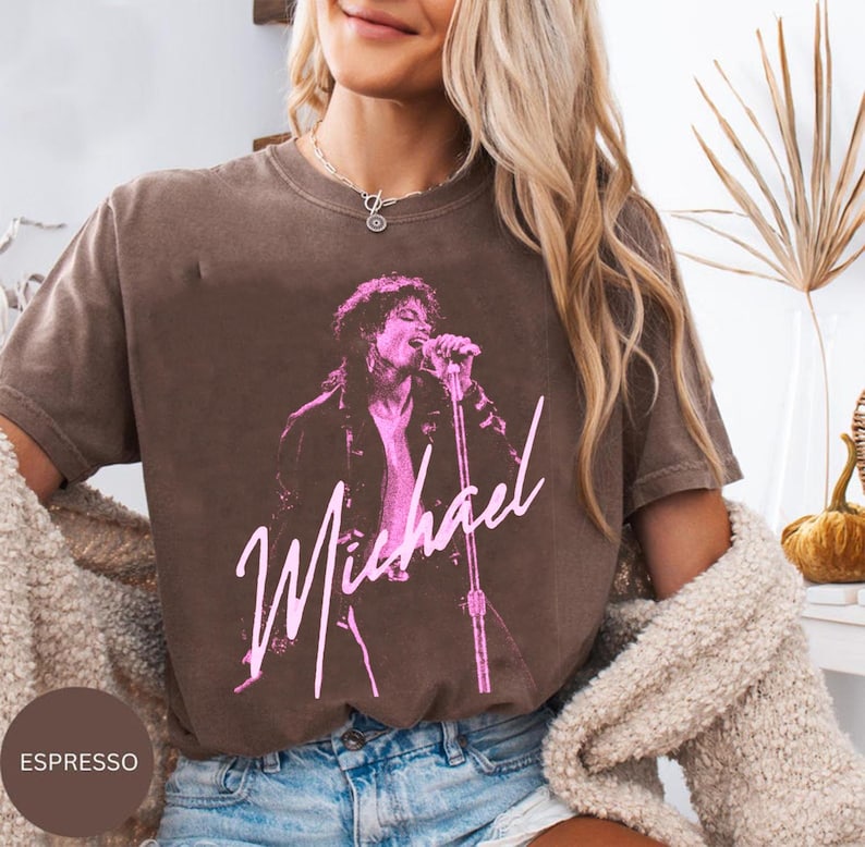 May include: Espresso-coloured t-shirt featuring a pink graphic of a singer with a microphone, with the name "Michael" in a cursive font. The shirt has a vintage, worn look.