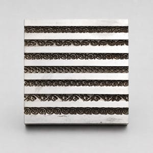 May include: A square silver-toned metal plate featuring six horizontal rows of embossed decorative patterns. Each row displays a distinct, intricate scrollwork or floral border design separated by smooth, flat, polished metal bands.