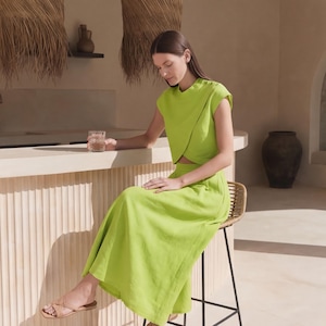 May include: A bright lime green two-piece set consisting of a short-sleeved, wrap-style crop top with a high neckline and a matching high-waisted, floor-length maxi skirt. The outfit is paired with simple tan slide sandals with thin straps.
