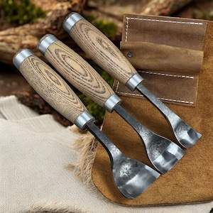 Peut inclure: Trois gouges à bois avec manches en frêne et viroles en métal reposent sur un étui à outils en cuir marron. Les gouges ont des lames incurvées pour la sculpture sur bois détaillée. Les manches présentent un motif de grain de bois naturel.