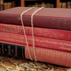 Puede incluir: Una pila de cuatro libros antiguos atados con cuerda. Los libros son de tonos rojos y burdeos, con letras doradas y patrones decorativos. Los títulos incluyen "Roget's Thesaurus of Words and Phrases" y "Glory Days With The Rodgers".