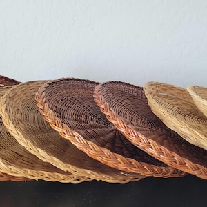 May include: A collection of round woven baskets in varying shades of brown and tan. The baskets have a braided edge and are arranged in a row, showcasing their natural textures and craftsmanship. The baskets are made of natural materials.