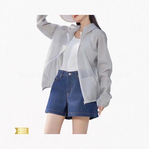 Puede incluir: Una chaqueta con capucha de manga larga en color gris claro, translúcida y con cremallera, sobre una camiseta blanca sin mangas y pantalones cortos de mezclilla azul oscuro. La chaqueta tiene una cremallera blanca y un tejido ligero.