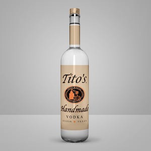 May include: A clear glass bottle of Tito's Handmade Vodka. The bottle has a tan label with black and orange text and a circular logo. The bottle is filled with a clear liquid and has a silver cap.