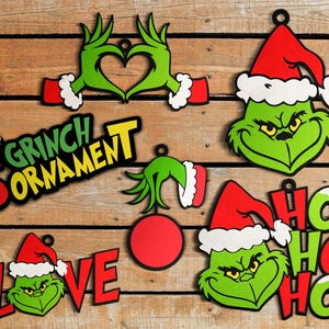 Könnte beinhalten: Eine Sammlung von Weihnachtsschmuck mit dem Grinch. Die Ornamente zeigen das Gesicht des Grinch, Hände, die ein Herz formen, und die Worte "Love" und "Ho Ho Ho". Der Text "5 Grinch Ornament" ist ebenfalls enthalten.