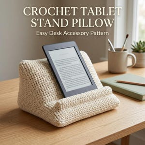 May include: A cream-colored crochet tablet stand pillow with a wedge shape, supporting a black e-reader. The text CROCHET TABLET STAND PILLOW Easy Desk Accessory Pattern is visible above the stand on a light background.