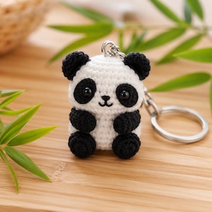 Può includere: Un piccolo portachiavi a forma di panda realizzato a mano all'uncinetto, con corpo bianco, orecchie, macchie intorno agli occhi, braccia e gambe nere. Il panda presenta due occhi in plastica nera lucida e un naso e una bocca ricamati in nero.
