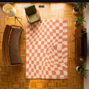 Könnte beinhalten: Draufsicht auf ein Wohnzimmer mit einem Teppich mit einem verzerrten Schachbrettmuster in Pfirsich und Weiß. Der Raum umfasst eine Holzbank, einen grünen Sessel, eine Stehlampe und einen Holzschrank mit einem Fernseher. Topfpflanzen sind im Raum platziert.