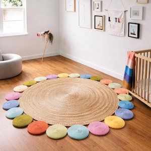 Könnte beinhalten: Ein runder Jute-Teppich mit konzentrischem Muster, umgeben von bunten, kreisförmigen gehäkelten Matten. Die Matten sind in den Farbtönen Rosa, Blau, Gelb, Grün und Orange gehalten. Der Teppich liegt auf einem Holzboden.
