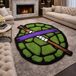 May include: A green and black rug shaped like a turtle shell, with a purple band and brown staff. The rug is placed on a gray carpet in a living room setting.