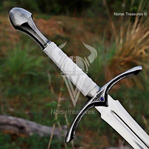 May include: A silver-colored sword with a white wrapped handle and a curved crossguard. The blade is shiny and the handle has a rounded pommel. A small blue gem is set into the crossguard. The text "Norse Treasures" is visible.