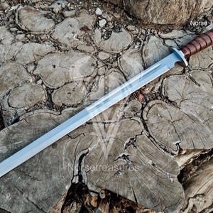 May include: A silver-colored sword with a brown leather-wrapped handle rests on a weathered wooden surface. The blade is long and straight, with a slight taper towards the tip. The handle is a rich brown, and the sword appears to be well-crafted.