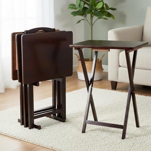 May include: Set of four dark brown folding TV trays. One tray is open, and the others are stacked. The trays have a rectangular tabletop and a folding X-frame base. A handle is on the top of the stacked trays. The trays are on a white rug.