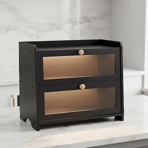 May include: A black two-tiered cabinet with glass doors and gold-colored knobs. The cabinet is made of wood and sits on a white countertop. The interior of the cabinet is illuminated with a warm light, creating a cozy atmosphere. The cabinet is designed for storage.