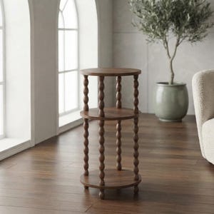 May include: A three-tier round wooden side table featuring a dark brown finish. The structure consists of three circular shelves supported by vertical legs with a distinct bobbin or spindle design, ending in small rounded feet at the base.