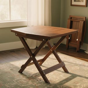 May include: A square, folding wooden table with a slatted top and an X-shaped leg design. The table is a dark brown color and appears to be made of wood. A second, folded table is visible in the background. The table measures approximately 24 inches wide.