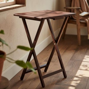 May include: A dark brown, folding side table with an X-shaped base and a square top. The table is made of wood and has a simple, classic design. The table is approximately 24 inches tall.
