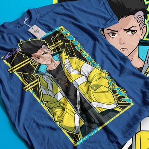 Pode incluir: Camiseta azul com um personagem de estilo anime usando uma jaqueta amarela e branca, uma camisa preta e um colar com uma cruz dourada. O design &eacute; emoldurado em amarelo e preto. Outra imagem do personagem &eacute; vis&iacute;vel.