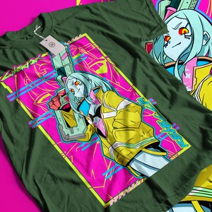 Op de afbeelding: Donkergroen t-shirt met een levendige afbeelding van een vrouwelijk anime-personage met blauw haar, rode ogen en een gele jas, die een futuristisch wapen vasthoudt. Het ontwerp staat tegen een roze en turquoise achtergrond met het woord "Cyberpunk" in neon groen.