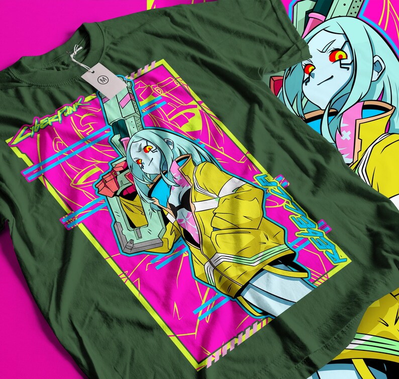 Op de afbeelding: Donkergroen t-shirt met een levendige afbeelding van een vrouwelijk anime-personage met blauw haar, rode ogen en een gele jas, die een futuristisch wapen vasthoudt. Het ontwerp staat tegen een roze en turquoise achtergrond met het woord "Cyberpunk" in neon groen.