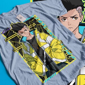 Pode incluir: Camiseta azul clara com um personagem de estilo anime usando uma jaqueta amarela e branca. O design inclui o rosto do personagem e um padr&atilde;o geom&eacute;trico com texto. Uma etiqueta est&aacute; presa &agrave; camiseta.