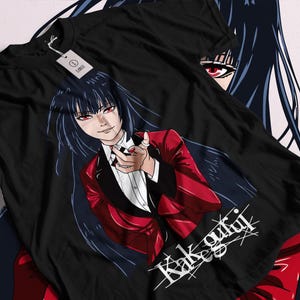 May include: Black t-shirt featuring a detailed anime illustration. The graphic depicts a character in a red suit with long black hair and red eyes. The text "Kakegurui" is displayed in white. A tag reads "LARGE".