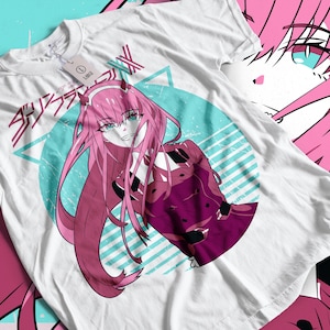 May include: White t-shirt with a pink-haired anime character design. The illustration features a character in a red outfit, set against a teal and white circular backdrop. Japanese text is also present.