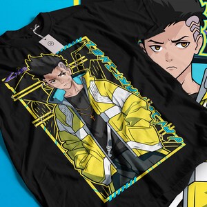 Pode incluir: Camiseta preta com uma ilustra&ccedil;&atilde;o em estilo anime de uma pessoa usando uma jaqueta amarela e branca. O gr&aacute;fico inclui o texto "ART IN WEST" em um design amarelo e azul. Uma etiqueta est&aacute; presa &agrave; camiseta.