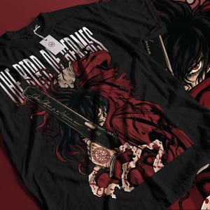 May include: A black t-shirt featuring a graphic illustration of a dark-haired character in a red coat holding a large black handgun. The text "THE BIRD OF HERMES" is printed in white above the character, and a red circular seal is visible on the hand.