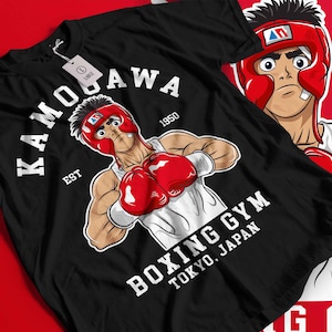 May include: Black t-shirt featuring a cartoon boxer in a red helmet and gloves. The shirt has the text "KAMOGAWA" and "BOXING GYM TOKYO, JAPAN" in white. The design includes the year "1950" and the word "EST".